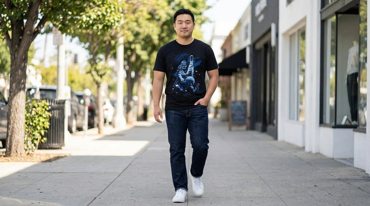 Man in the Cosmic Descent graphic tee with dark jeans and white sneakers walking down a tree-lined street